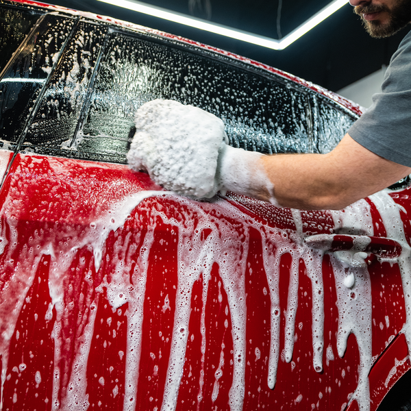 Red car detail: Man washes vehicle with a sudsy mitt. Auto detailing. Car care.